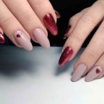 Яркий сияющий красный маникюр с небольшим рисунком сердечка на длинных ногтях миндальной формы