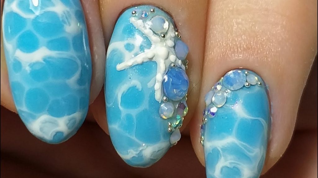 Идея оформления ногтей в голубом цвете с узором Волны, декоративными камнями и объемной морской звездой
