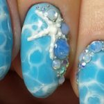 Идея оформления ногтей в голубом цвете с узором Волны, декоративными камнями и объемной морской звездой