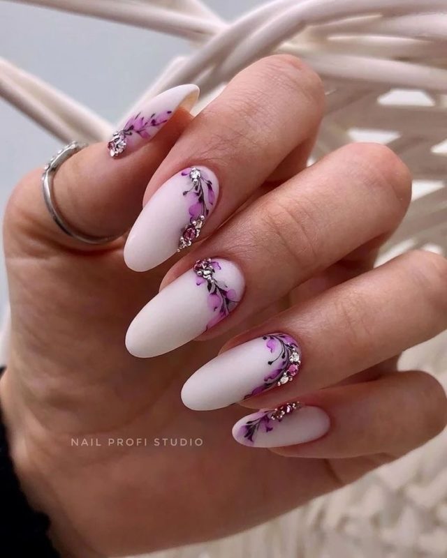 Весенний маникюр в белом цвете с фиолетовыми цветочными рисунками с блестящими аксессуарами