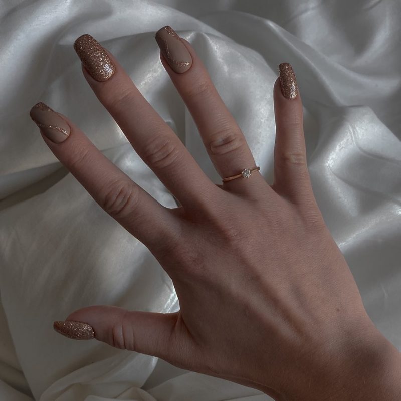 Длинные квадратные ногти бежевого цвета с золотистыми вставками, дополненные глиттером