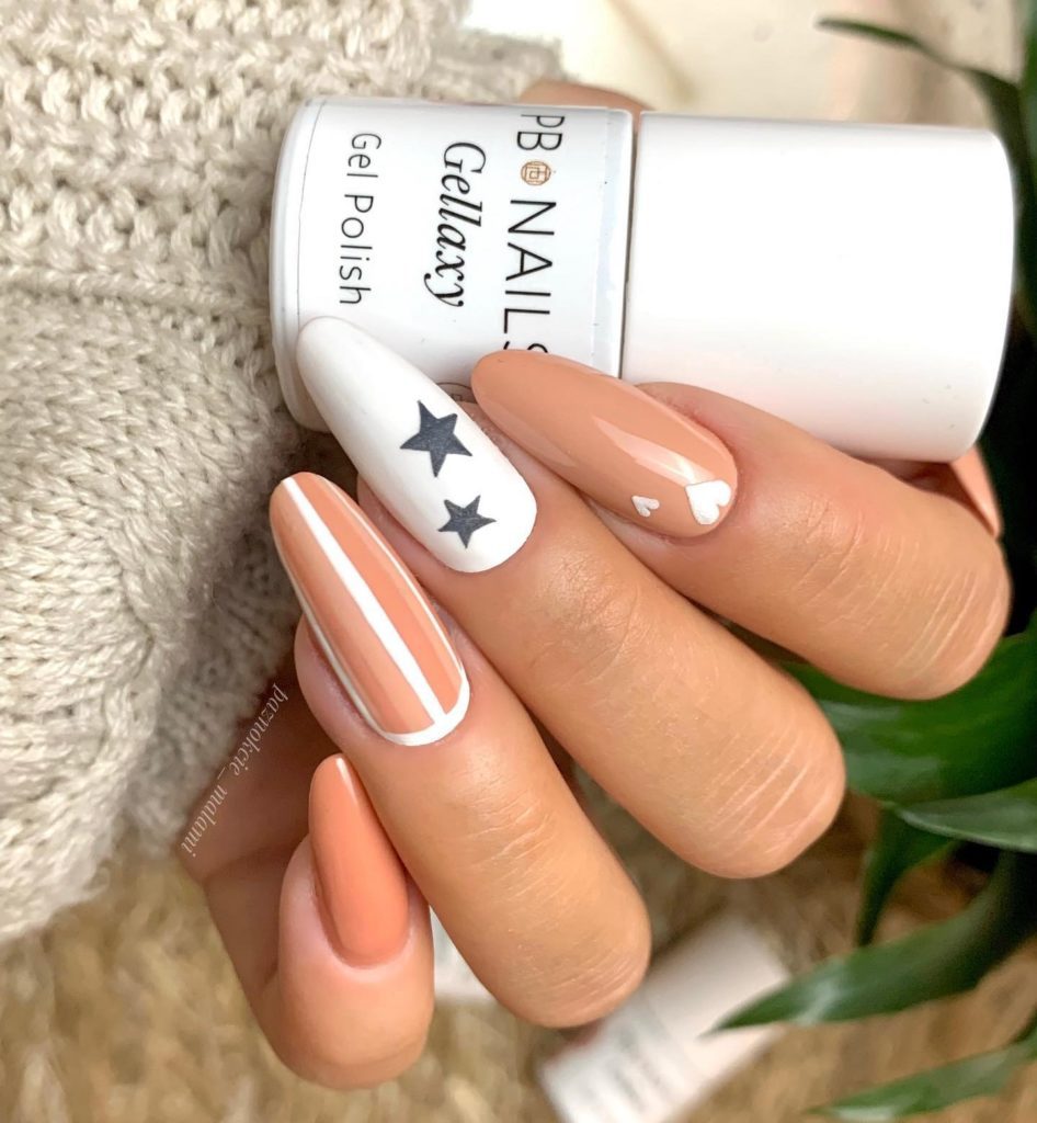 Бежево-персиковые ногти с вставками белого цвета, темными звездами и сердечками разного размера