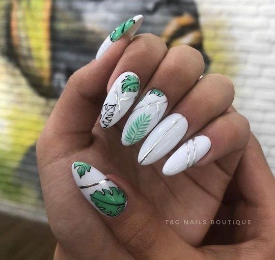 Белоснежный дизайн ногтей миндалевидной формы с зелеными рисунками листьев и серебристыми полосками
