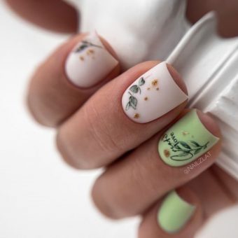 Квадратные короткие ногти в молочном и фисташковом цвете с маленькими рисунками листьев и вкраплением потали