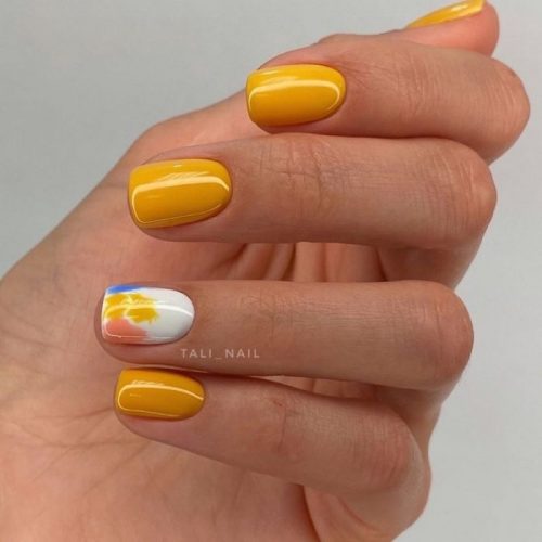 Насыщенно-желтое оформление ногтей с белым оформлением и яркими пятнами на безымянном пальце